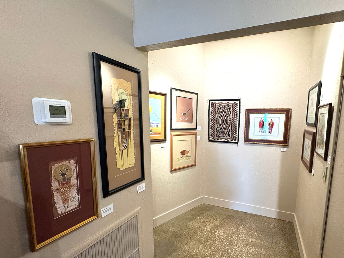Corner of gallery filled with paintings and weavings displayed on the walls