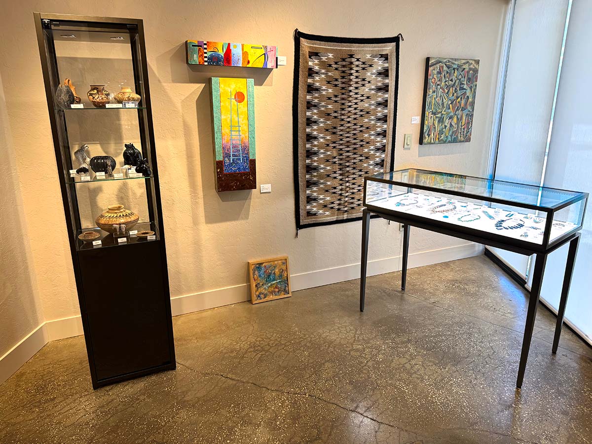 Glass display of ceramics, paintings and weaving on wall and glass case of jewelry