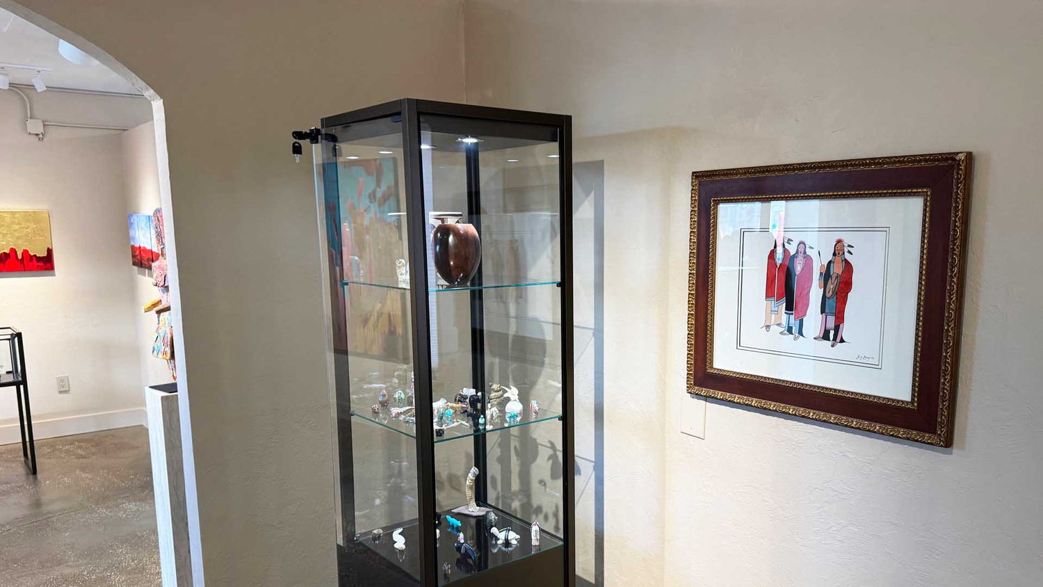Glass display cabinet with decorative items in a room with framed artwork on the wall.